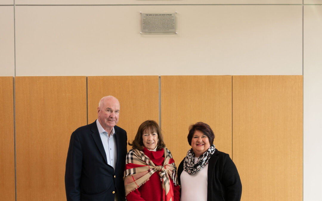 Mr. Michael Weir, Mrs. Suellen Weir, and Dean Wilkinson stand in front of a photo of the Weirs in the new Weir Atrium located in Williamson Hall on YSU's campus.