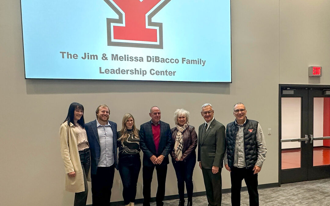 Family standing in front of a projection that says "The Jim and Melissa DiBacco Leadership Center".
